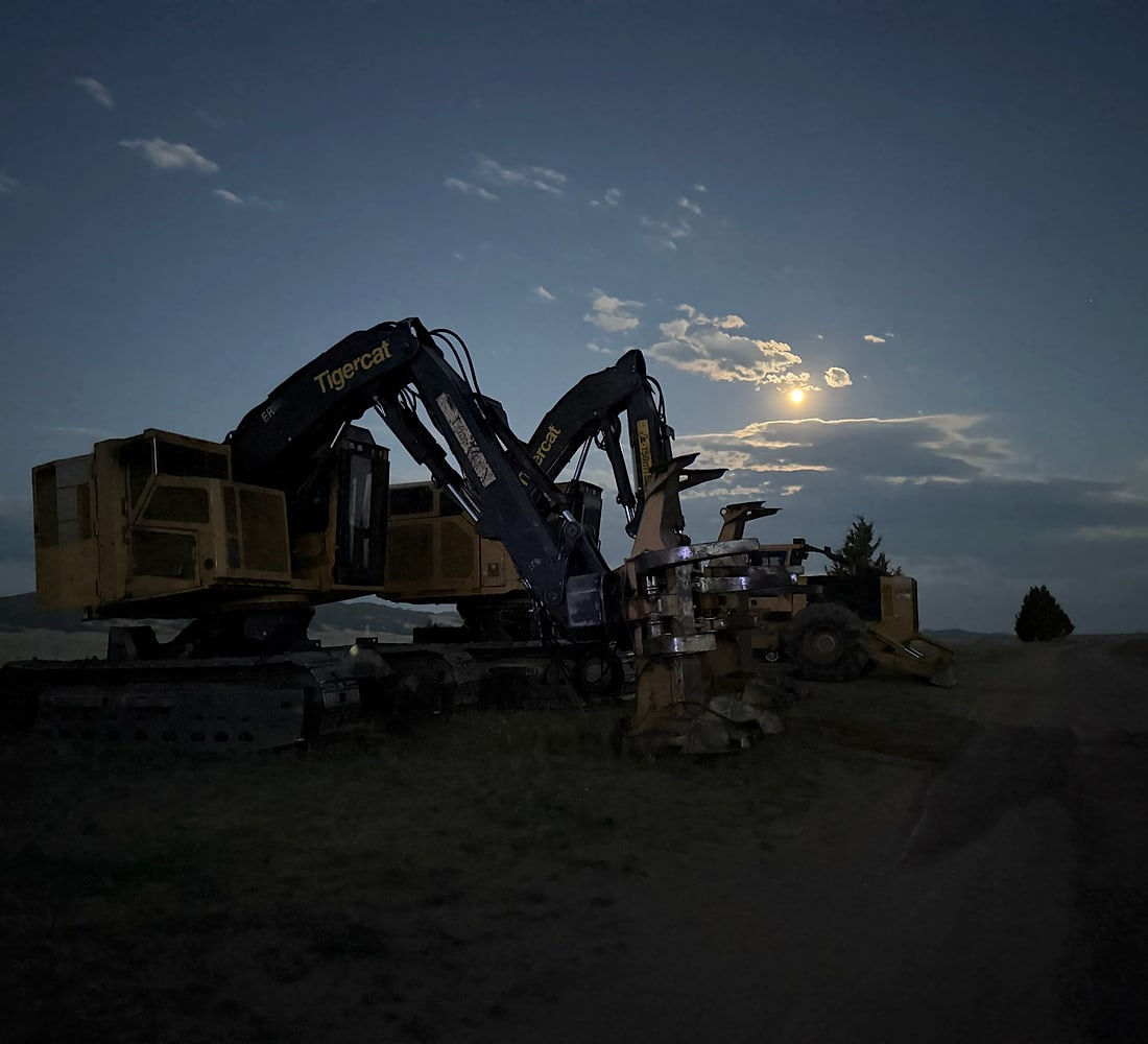 Over The Top's Tigercat feller buncher and skidder parked on a Montana ridge as the moon rises